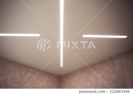 Modern designer stretch ceiling with illuminated LED lines in the room, backlighting Modern designer stretch ceiling with illuminated LED lines in the room, backlighting 128865940