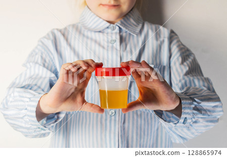 A child holds a urine test in his hands. The concept of sand in the kidneys in children, protein in the urine. Pediatric urology, close-up 128865974