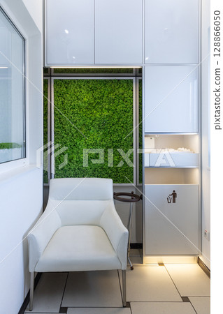 Modern and Minimalistic Waiting Area Featuring a White Chair and Lush Green Wall Decor Adds a Touch of Nature to the Interior Design of the Space Modern and Minimalistic Waiting Area Featuring a White Chair and Lush Green Wall Decor Adds a Touch of Nature to the Interior Design of the Space 128866050
