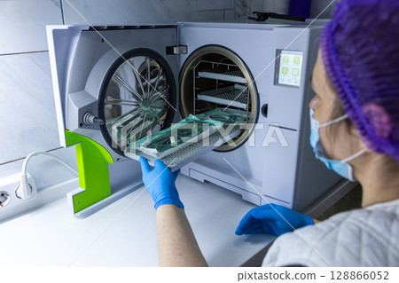 A Healthcare Professional Using a Modern Autoclave for Sterilization in a Clinical Setting with Safety Gear, Emphasizing Hygiene and Patient Safety Measures A Healthcare Professional Using a Modern Autoclave for Sterilization in a Clinical Setting with Safety Gear, Emphasizing Hygiene and Patient Safety Measures 128866052