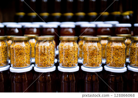 Rows of golden bee pollen jars with honey containers in background Rows of golden bee pollen jars with honey containers in background 128866068