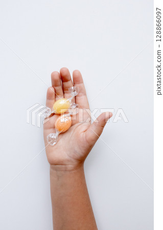 Child hand holding wrapped candy in a caucasian young hand on white background 128866097