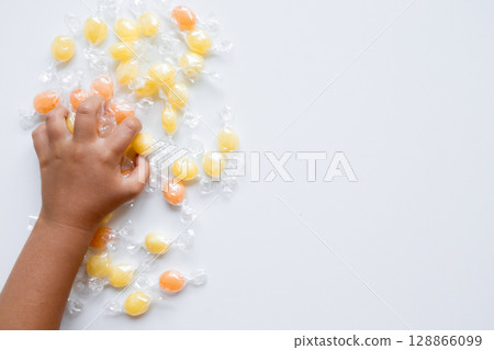 Child hand reaching for assorted wrapped candies on white background 128866099