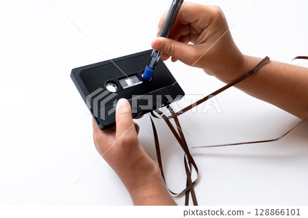 Hands repairing audio cassette tape with pen on white background Hands repairing audio cassette tape with pen on white background 128866101