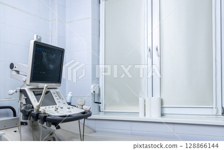 Medical Ultrasound Equipment in a Brightly Lit Examination Room with a Window Covered for Privacy and a Clean, Sterile Environment for Patient Comfort and Safety 128866144