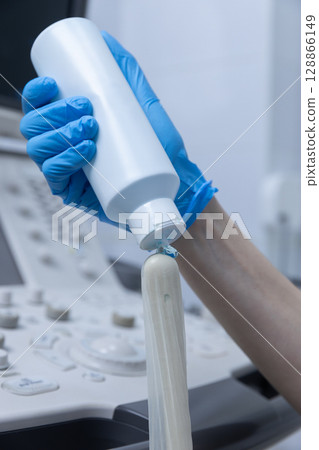 A Close-Up Image of a Medical Professional Using a Bottle to Prepare a Transducer for an Ultrasound Examination in a Clinical Setting with Advanced Medical Equipment A Close-Up Image of a Medical Professional Using a Bottle to Prepare a Transducer for an Ultrasound Examination in a Clinical Setting with Advanced Medical Equipment 128866149