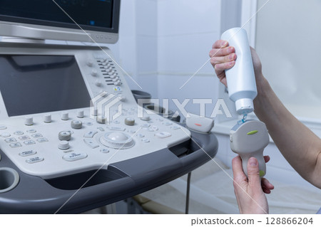 Ultrasound Machine Setup: A Professional Preparing the Transducer with Gel at a Medical Facility for Diagnostic Imaging and Patient Assessment Using Modern Equipment 128866204
