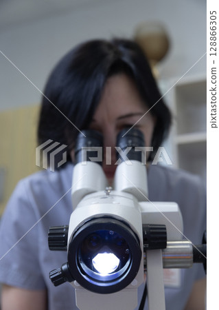 A dedicated laboratory technician intently observing samples through a high-powered microscope, showcasing the precision and detail involved in microscopic examination and research. 128866305
