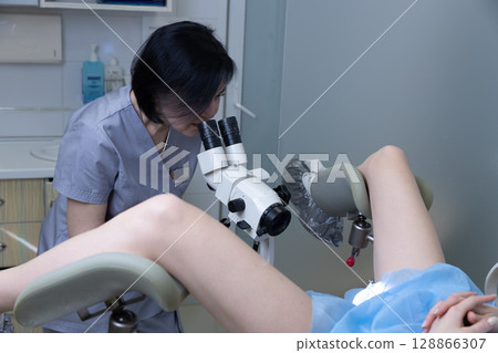 A Healthcare Professional Conducts a Close Examination Using a Microscope as a Patient Receives Care in a Medical Facility, Ensuring Quality Healthcare Services are Provided. A Healthcare Professional Conducts a Close Examination Using a Microscope as a Patient Receives Care in a Medical Facility, Ensuring Quality Healthcare Services are Provided. 128866307