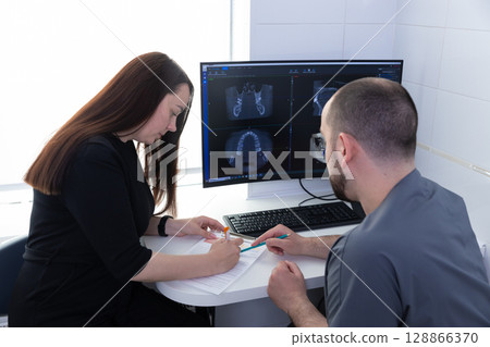 A Professional Consultation on Dental Health: A Patient Discusses Treatment with a Dentist While Reviewing X-ray Results on a Computer Screen 128866370