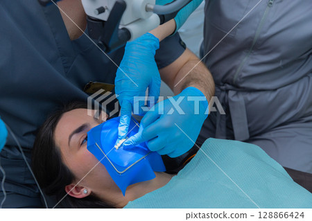 Dental Procedure in Action: A Close-Up of Dental Treatment with Blue Isolation Sheet and Professional Care by Dentists for Patient Oral Health Enhancement 128866424