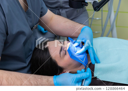 Professional Dental Care: A Dentist Performing an Oral Procedure While a Patient Receives Treatment with Precision and Comfort in a Modern Dental Clinic Setting 128866464