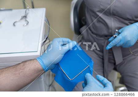 Dental Procedure in Progress: A Close-Up of a Dentist Preparing Equipment and Patient for Treatment with Focus on Sterile Environment and Professionalism Dental Procedure in Progress: A Close-Up of a Dentist Preparing Equipment and Patient for Treatment with Focus on Sterile Environment and Professionalism 128866466