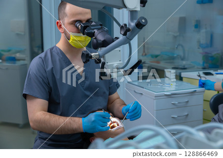Professional dentist performing a dental procedure with surgical microscope, ensuring precision and care during patient treatment in a modern dental clinic environment. 128866469