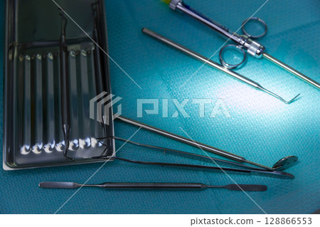 A Close-Up View of Surgical Instruments on a Blue Surgical Drape with Glare Highlighting Their Steel Surface and Reflected Smoothness in a Medical Environment Setup 128866553