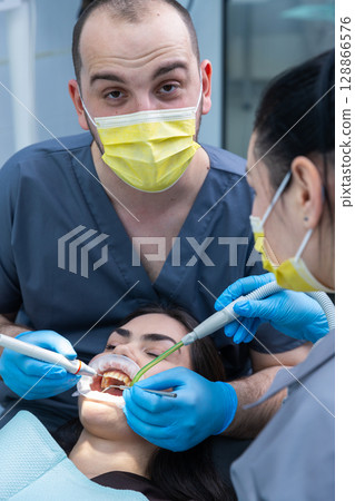 Dental Care in Action: Professional Team Performing a Routine Treatment with Advanced Tools and Techniques for Patient Comfort and Oral Hygiene 128866576
