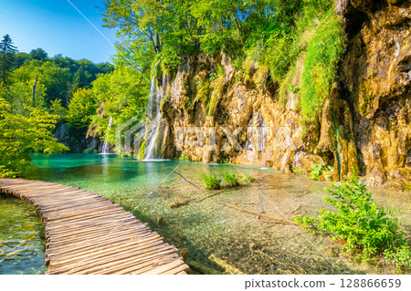 Wooden footpath at Plitvice national park, Croatia. Pathway in the forest near the lake and waterfall. Fresh beautiful nature, peaceful place. Famous tourist destination. Wooden footpath at Plitvice national park, Croatia. Pathway in the forest near the lake and waterfall. Fresh beautiful nature, peaceful place. Famous tourist destination. 128866659