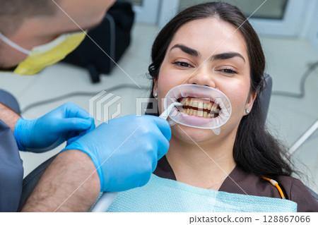 Patient Smiling in Dental Clinic During Oral Check-Up with Hygienist Using Tools for Cleaning and Examination, Highlighting Dental Hygiene and Patient Comfort. 128867066