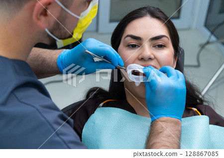 Professional Dental Care: Dentist Examining Patient's Teeth with Tools While Wearing Gloves and Mask in Modern Clinic Setup for a Healthy Smile. 128867085
