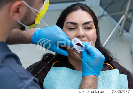 Dental Professional in Blue Gloves Performing Oral Examination on Patient in Clinic Setting with Protective Measures for Safety and Hygiene Practices 128867087