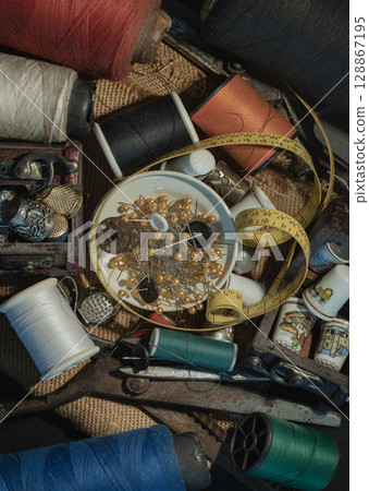 Spools of thread of various colors, Thimbles in small wooden treasure chest, Steel scissors, Sewing needles stuck in a green miniature spools thread and Measuring tape including pins in small round Spools of thread of various colors, Thimbles in small wooden treasure chest, Steel scissors, Sewing needles stuck in a green miniature spools thread and Measuring tape including pins in small round 128867195