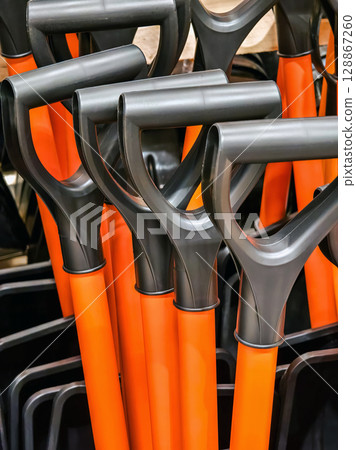Collection of orange shovels displayed for sale at a hardware store during daylight hours 128867260