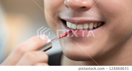 Beauty Routine. Male applying red lip gloss for a stylish look. 128868631