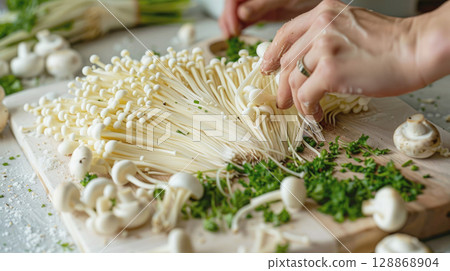 Close Up female hands preparing fresh enoki mushrooms with chopped parsley on a wooden cutting board. Cooking process, vegetarian ingredients and kitchen vibes Close Up female hands preparing fresh enoki mushrooms with chopped parsley on a wooden cutting board. Cooking process, vegetarian ingredients and kitchen vibes 128868904