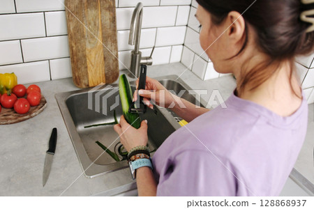 Woman In The Kitchen Peeling Cucumbers For A Fresh Vegetable Salad Woman In The Kitchen Peeling Cucumbers For A Fresh Vegetable Salad 128868937