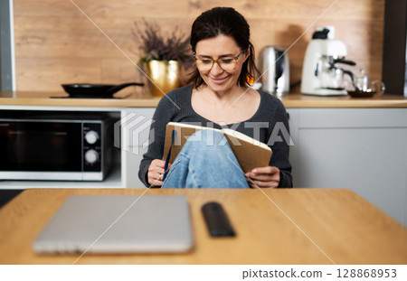 Young Woman In Kitchen Reading Notes In Notepad Young Woman In Kitchen Reading Notes In Notepad 128868953