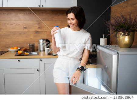 Joyful Woman On The Kitchen Grabbing Milk Bottle From Fridge 128868964