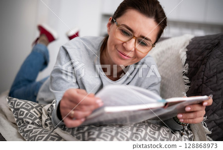 Happy Young Woman Reads An Interesting Modern Novel At Home Happy Young Woman Reads An Interesting Modern Novel At Home 128868973