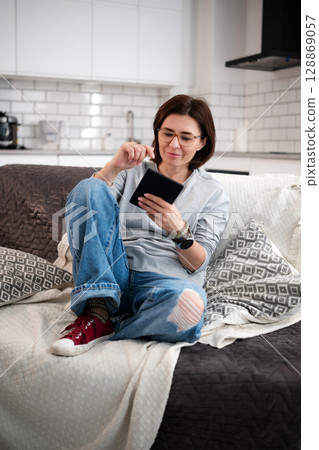 Woman Sitting On Sofa Reading E-Book At Home Woman Sitting On Sofa Reading E-Book At Home 128869057