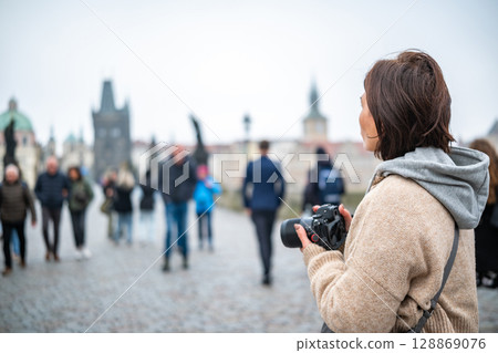 Female Photographer Taking Photos On Charles Bridge In Prague Among The Tourist Crowd 128869076