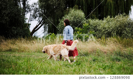 Woman Walks On A Green Lawn With A Golden Retriever 128869098