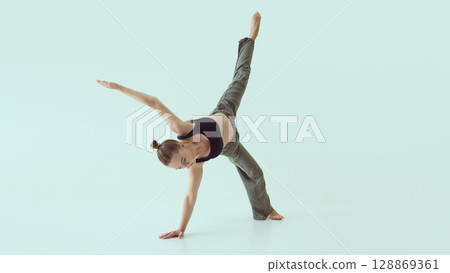 Female dancer holding one-arm floor balance with extended leg and intense focus 128869361
