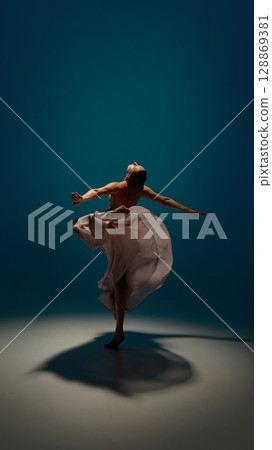 Dance and reflection. Graceful young woman spinning in mid-air with dramatic motion and flowing skirt under spotlight Dance and reflection. Graceful young woman spinning in mid-air with dramatic motion and flowing skirt under spotlight 128869381