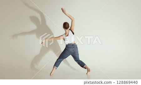 Inner voice. Young dancer captured from behind mid contemporary movement with dramatic shadow on wall 128869440