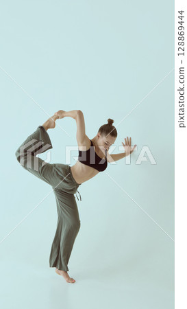 Contemporary dancer balancing in standing pose with focused expression against pale background 128869444