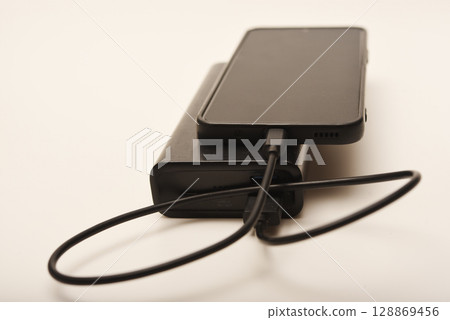 Charging a mobile phone from a powerbank. Charging the gadget. Charging a mobile phone from a powerbank. Charging the gadget. 128869456