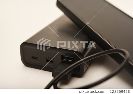 Charging a mobile phone from a powerbank. Charging the gadget. Charging a mobile phone from a powerbank. Charging the gadget. 128869458