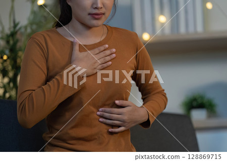 Health Awareness: Young woman feeling abdominal discomfort at home 128869715