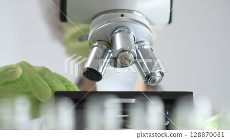 Close up of green gloved hands of a scientist adjusting a microscope in a laboratory, emphasizing the significance of scientific research and analysis. Medicine, healthcare and science concept Close up of green gloved hands of a scientist adjusting a microscope in a laboratory, emphasizing the significance of scientific research and analysis. Medicine, healthcare and science concept 128870081