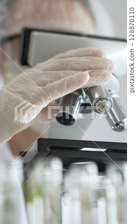 Close up of white gloved hand of a scientist adjusting a microscope in a laboratory. Medicine, health care and science concept Close up of white gloved hand of a scientist adjusting a microscope in a laboratory. Medicine, health care and science concept 128870110