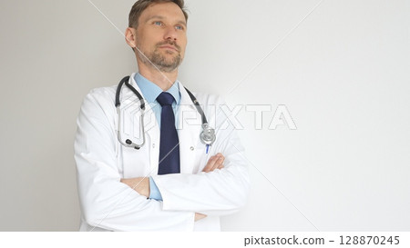 Headshot of a confident doctor man wearing stethoscope and white coat, is standing with crossed arms, representing medical professionalism and expertise. Medicine and health care Headshot of a confident doctor man wearing stethoscope and white coat, is standing with crossed arms, representing medical professionalism and expertise. Medicine and health care 128870245