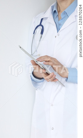 Unknown female doctor, wearing white coat over a blue blouse and a stethoscope, is using a digital tablet, suggesting innovative healthcare practices in medicine. Health care and medicine concept Unknown female doctor, wearing white coat over a blue blouse and a stethoscope, is using a digital tablet, suggesting innovative healthcare practices in medicine. Health care and medicine concept 128870264