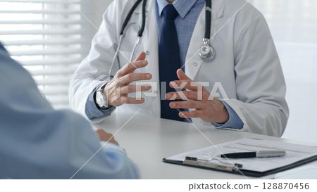 Medical professional explaining diagnosis, gesturing hands to patient during consultation in well lit clinical setting. Medicine and health care concept 128870456