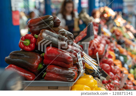 Raw juicy red bell pepper and vegetables on display at a food market. Selective focus on sweet pepper. Paprika Raw juicy red bell pepper and vegetables on display at a food market. Selective focus on sweet pepper. Paprika 128871141