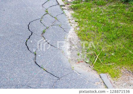 This is a closeup view of a cracked asphalt road near a grassy area 128871536