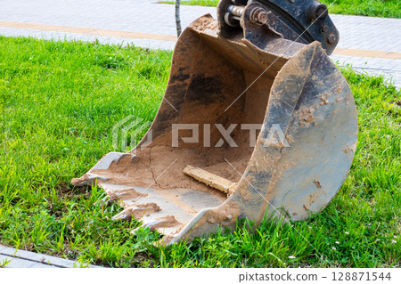 A large excavator bucket is currently resting in the grass nearby A large excavator bucket is currently resting in the grass nearby 128871544